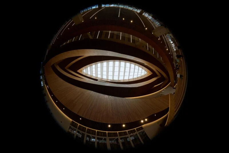 A fisheye view looking up at a multi-story atrium with curved wooden walls and a central oval skylight.