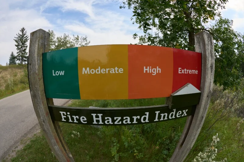 A Fire Hazard Index sign stands outdoors, featuring a color-coded scale from green (Low) to yellow (Moderate), orange (High), and red (Extreme).