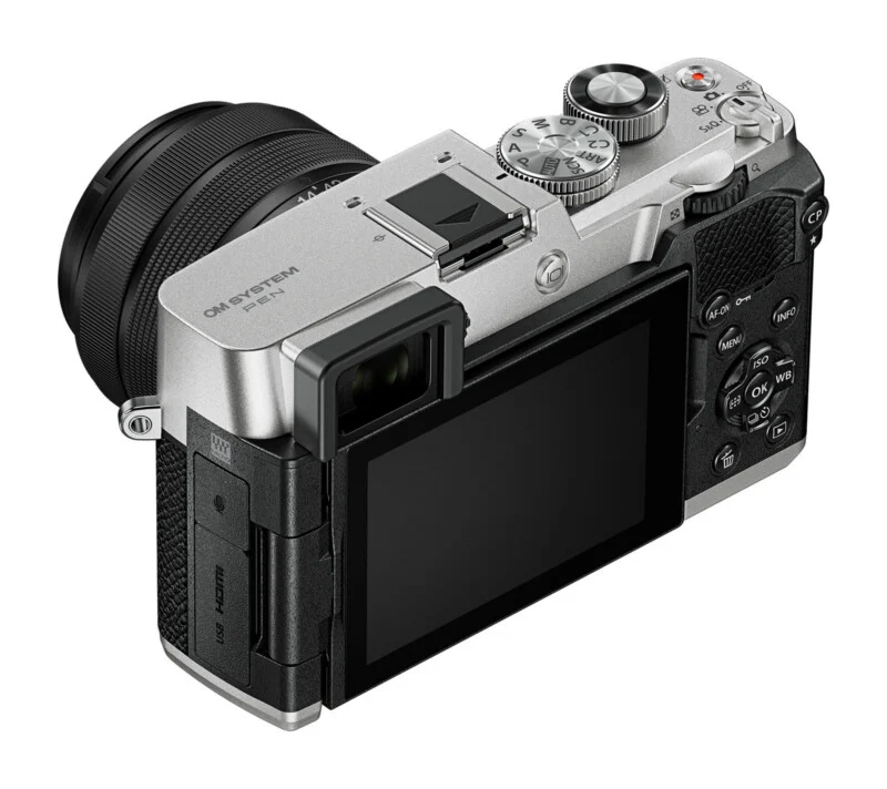 A silver and black mirrorless digital camera with an attached lens, viewed from the rear angle, showing the screen, buttons, and top dials.