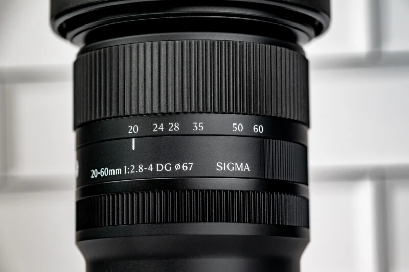 A close-up view of a black Sigma 20-60mm camera lens, showing the focal length markings and the 67mm filter thread diameter.
