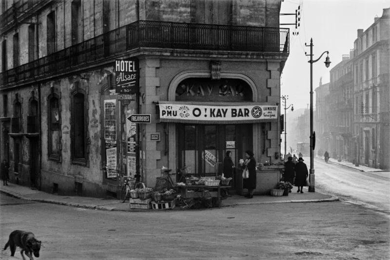 A black-and-white street scene shows a corner building housing the