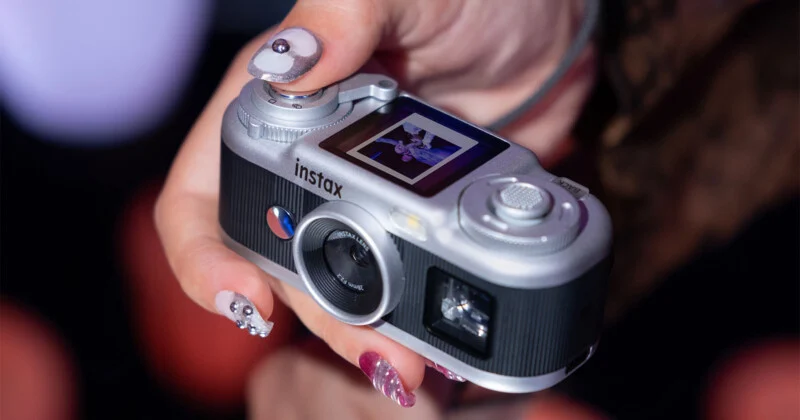 Een persoon houdt een zilveren en zwarte Instax-camera vast terwijl hij een korte foto op diens achter het scherm toont.