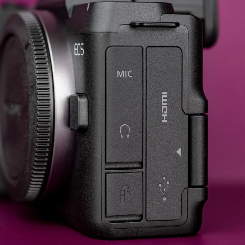 Een close-up van de zijkant van een zwarte camerabehuizing, met rubberen poorten gemerkt voor een microfoon, hoofdtelefoon, afstandsbediening, HDMI en USB.