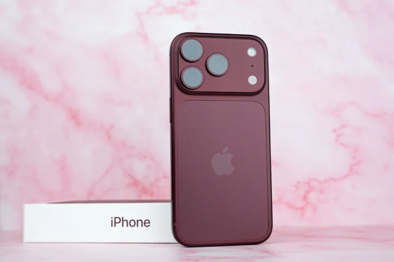 Een donkerrode smartphone staat rechtop voor zijn witte doos op een roze marmeren oppervlak.