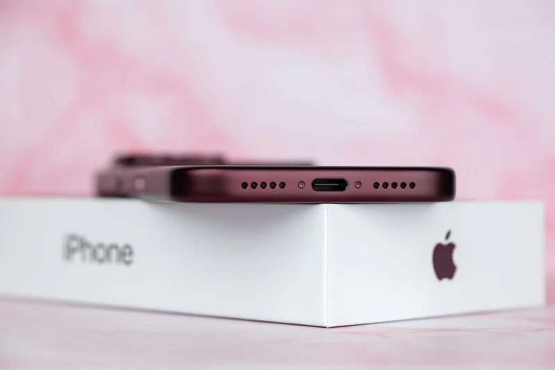 Een donkerrode smartphone rust bovenop een witte iPhone-doos tegen een roze marmeren achtergrond.