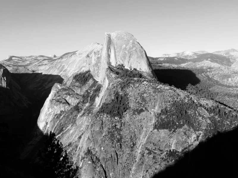 Een zwart-wit landschapsbeeld van Half Dome met zijn pure granietwand die uitsteekt boven een bosachtige bergkam.
