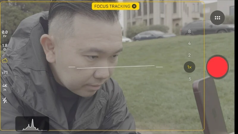 Een smartphone-camera-interface toont een persoon in een donker jack die naar beneden kijkt, met tracking en een histogram zichtbaar onderaan.
