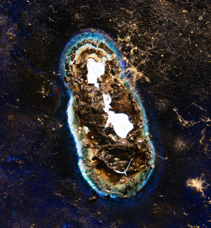 A dark, textured surface features a central, irregular hole surrounded by a vibrant blue and white ring, with scattered light-colored fibers across the background.