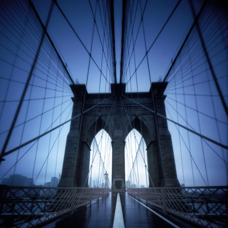 A symmetrical, low-angle view of the Brooklyn Bridge stone towers and suspension cables under a deep blue sky.