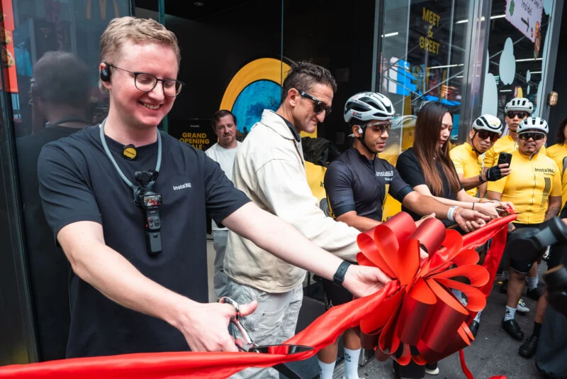 A group of people, including Casey Neistat, cut a large red ribbon during a store opening event.