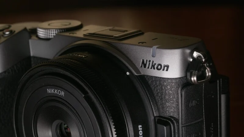 A close-up view of a silver and black Nikon Z fc mirrorless camera body with a Nikkor lens attached.