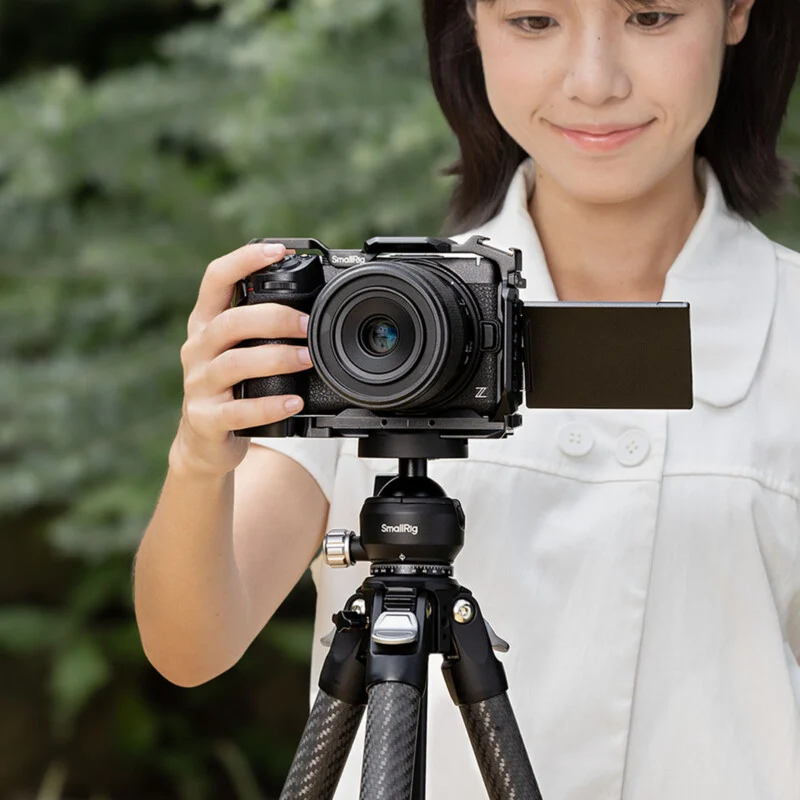 A woman in a white shirt holds a camera mounted on a SmallRig tripod, with the camera's side screen flipped out.