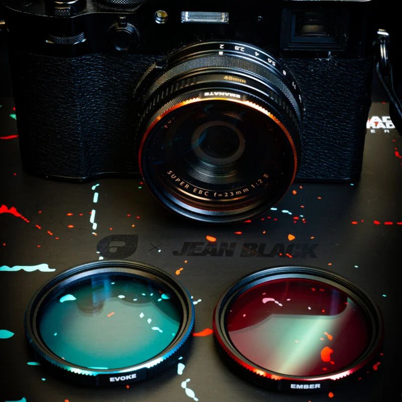 A black camera with a 23mm lens sits above two circular camera filters, one teal labeled 