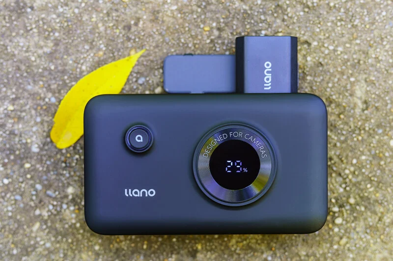 A black Llano portable power bank with a digital display showing 29% battery sits on a textured ground surface next to a yellow leaf.