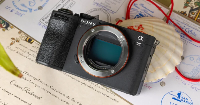 A black Sony Alpha 7C camera body sits on a surface covered with stamped documents and a scallop shell.