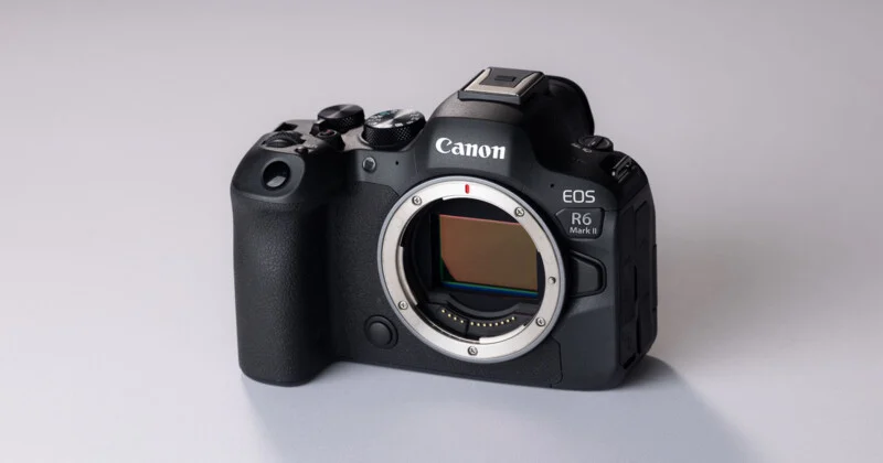 A black Canon EOS R6 Mark II mirrorless camera body sits on a light gray surface, showing the lens mount and sensor.