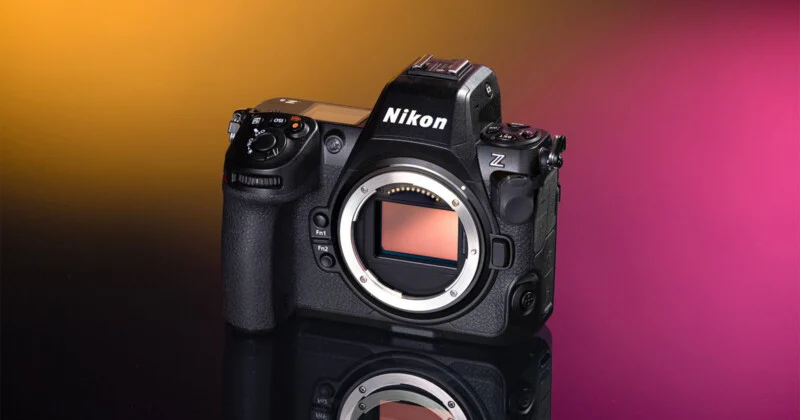 A black Nikon Z 8 mirrorless camera body sits on a reflective surface against a gradient yellow and magenta background.