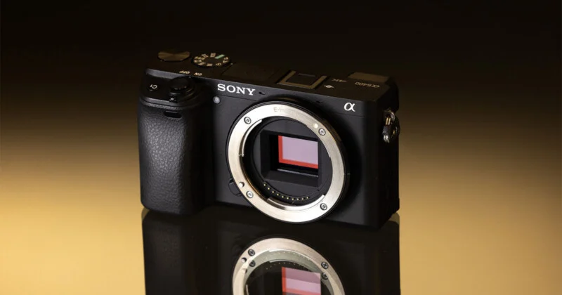 A black Sony Alpha 6400 mirrorless camera body sits on a reflective surface against a gradient brown background.