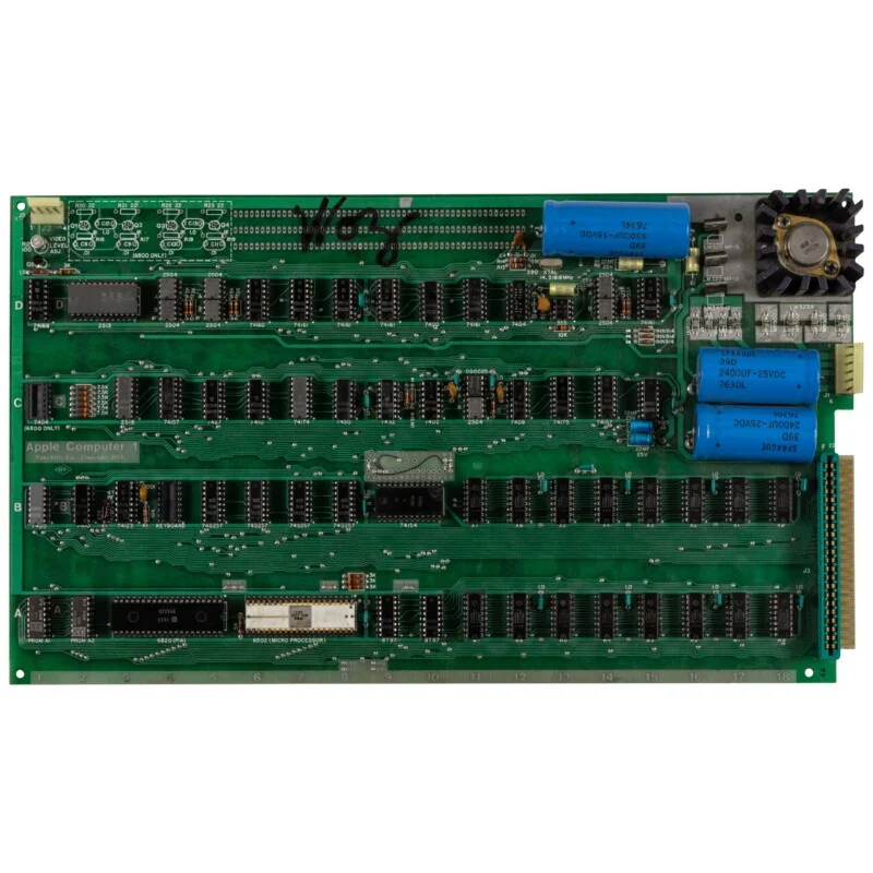 An Apple-1 computer circuit board featuring a 6502 microprocessor, rows of integrated circuits, capacitors, and a heat sink.