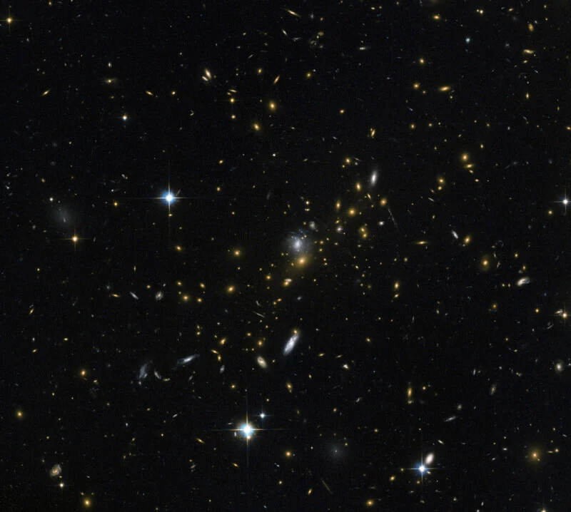 A dense field of distant galaxies of various shapes and sizes, interspersed with several bright, spiked foreground stars.