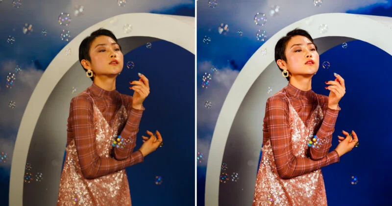 A person with short dark hair wearing a plaid long-sleeved top and a sequined dress poses in front of a circular archway surrounded by floating bubbles.