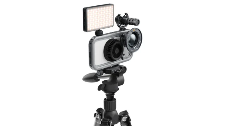 A smartphone mounted in a protective cage on a tripod, equipped with an external LED light, a microphone, and a lens attachment.