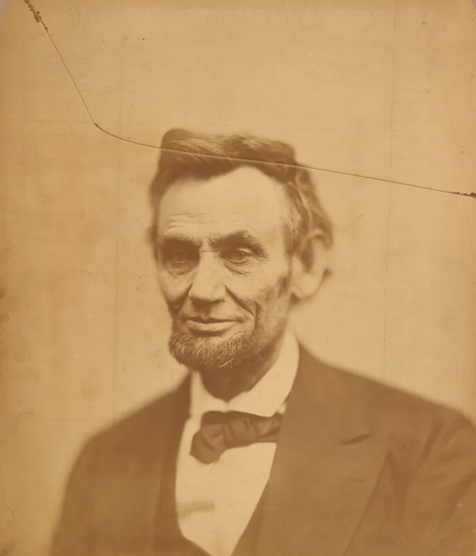 A sepia-toned portrait of Abraham Lincoln, showing his head and shoulders, with a prominent diagonal crack across the top.