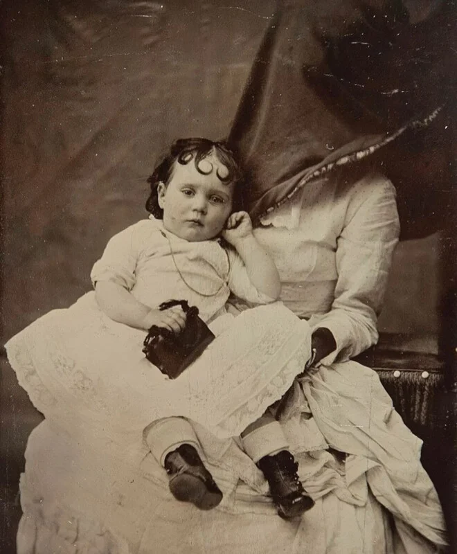 hidden mother style portrait of a young child and her mother, whose face is obscured by a cloth