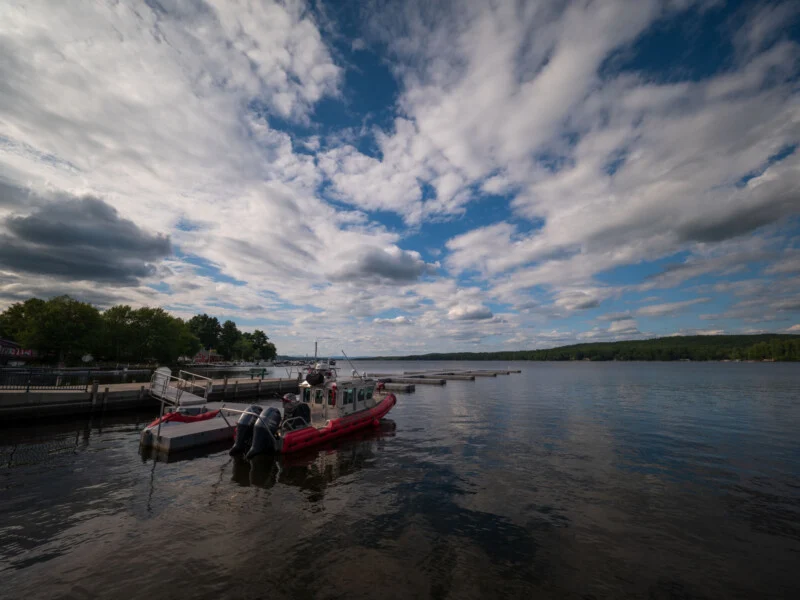 A red and white emergency response boat is docked at a pier on a calm lake under a cloudy sky.