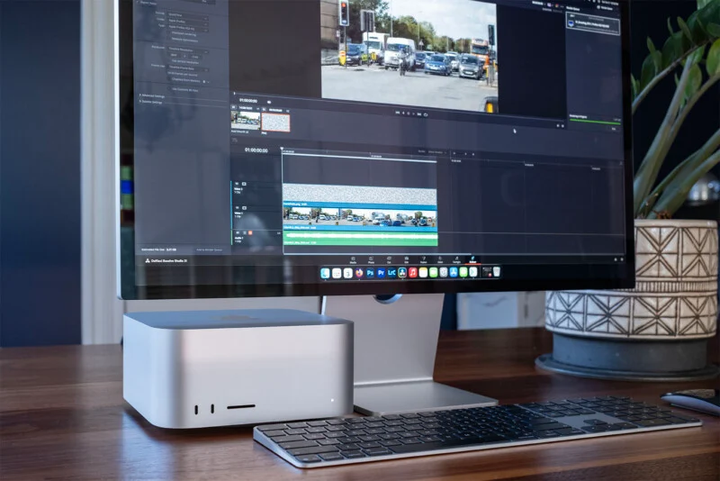 A Mac Studio computer sits on a wooden desk next to a monitor displaying the DaVinci Resolve video editing interface.