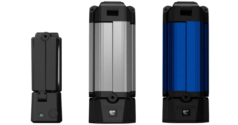 Three portable, cylindrical LED light fixtures stand side-by-side, featuring a small black unit on the left and two larger silver and blue units on the right with digital displays.