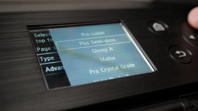 A close-up of a printer's digital menu screen displaying paper type options, with "Plus Semi-gloss" currently highlighted.